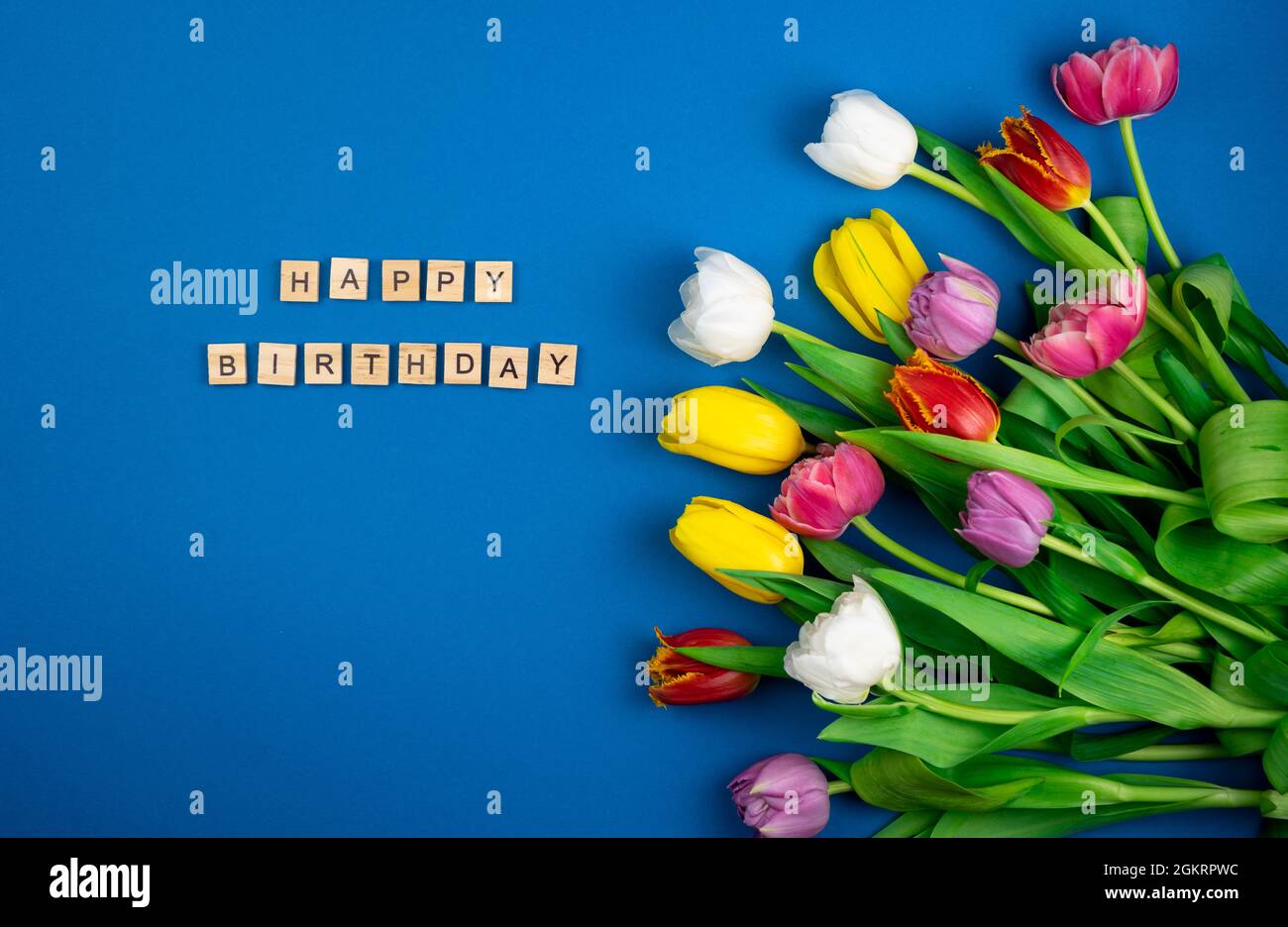 Buon compleanno l'iscrizione in lettere di legno. Mix di tulipani primaverili fiori. Sfondo con fiori tulipani primo piano diversi colori. Multi Foto Stock