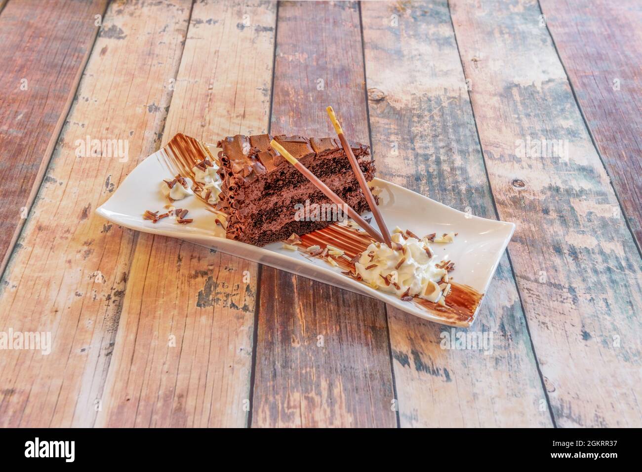 Morte per dessert al cioccolato su un piatto rettangolare bianco con panna e bastoncini di cioccolato Foto Stock