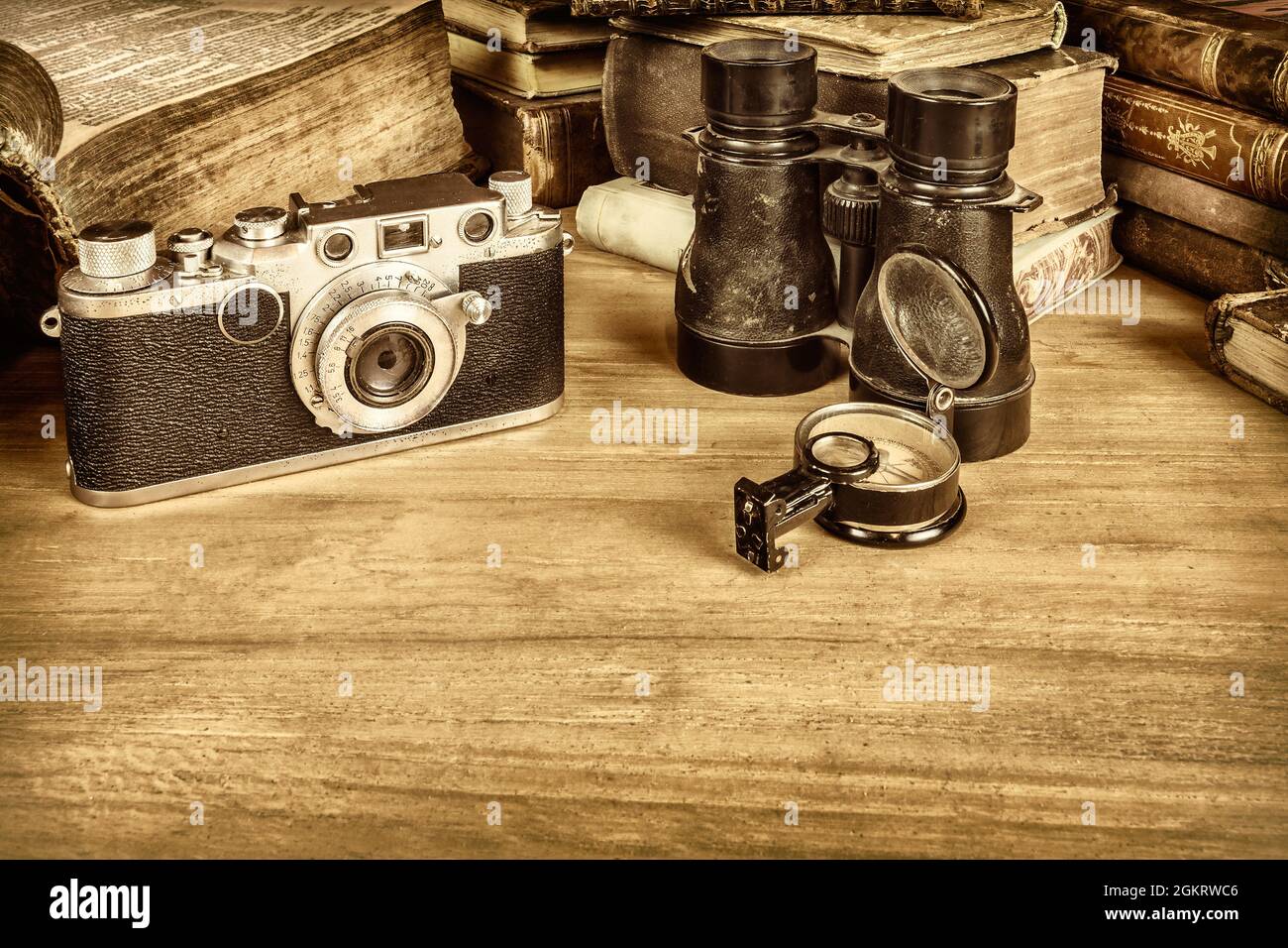 Immagine in stile seppia di un tavolo in legno con vecchi libri, macchina fotografica, binoculare e bussola Foto Stock