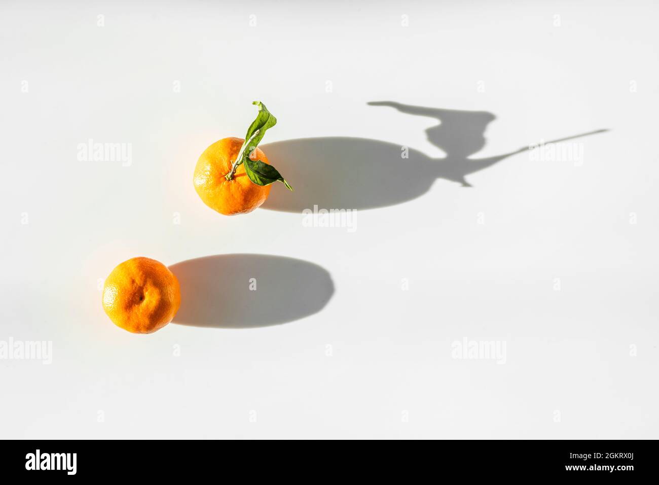 due tangerini al sole che creano un'ombra laterale allungata e dura Foto Stock