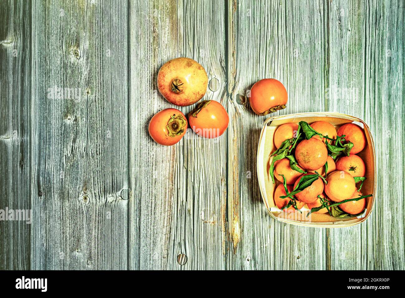 Immagine dall'alto di cesto di legno con frutta matura, mandarini con foglie verdi, persimmoni e melograno su tavole di legno Foto Stock