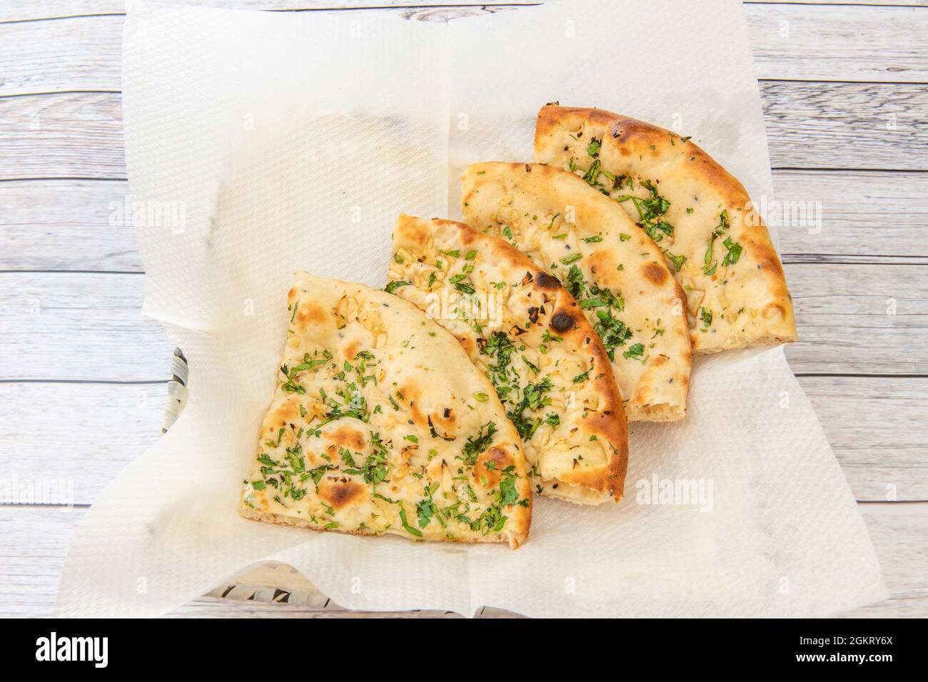 Porzioni di pane tradizionale all'aglio di naan indù su carta assorbente e un sacco di prezzemolo su tavola bianca Foto Stock