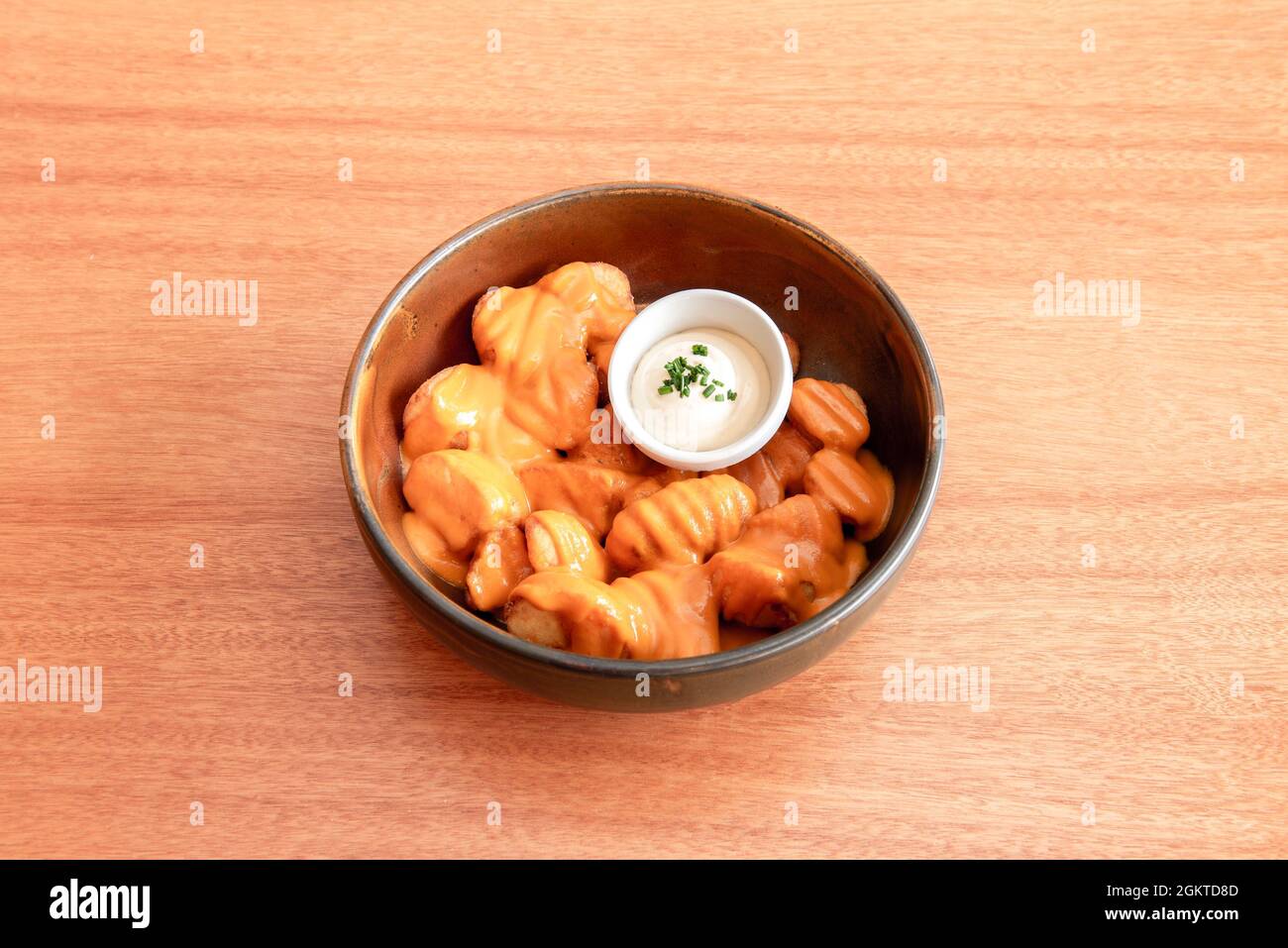 Fantastica porzione di patatas bravas a la Madrid con salsa piccante e maionese con erba cipollina tritata su un tavolo di legno di ciliegio Foto Stock