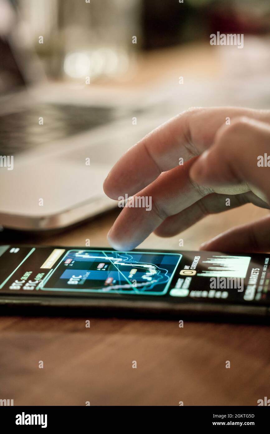 Un uomo d'affari che controlla la criptovaluta e i prezzi delle azioni su un'app mobile a casa. Investire utilizzando uno smartphone online. Foto Stock