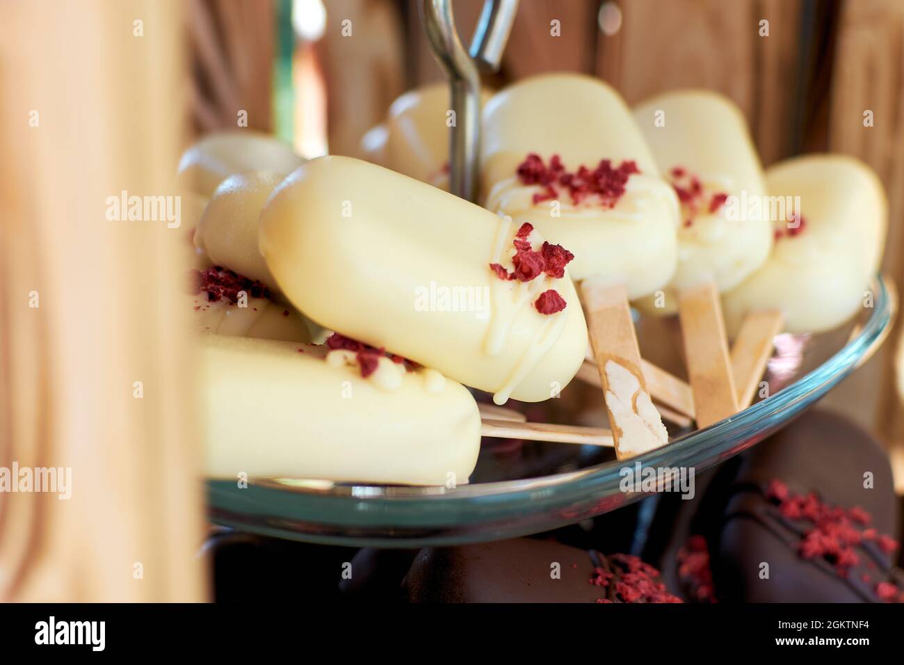 La torta si schiaccia di cioccolato bianco a forma di un mini gelato su un bastone. I cippoli di torta sono guarniti con briciole secche di fragola. Messa a fuoco selettiva. Foto Stock