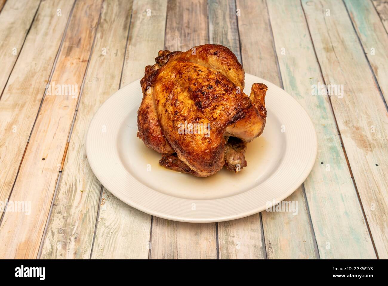 Pollo intero arrostito in una rotisserie con pelle molto croccante su piatto bianco e tavolo in legno Foto Stock