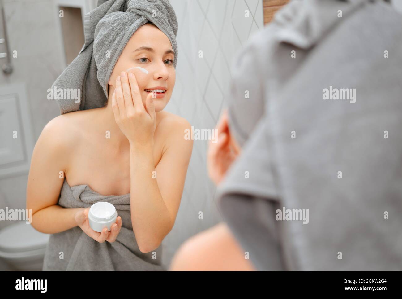 Donna lo specchio spalma la crema sulla guancia dalle rughe e dalla vecchiaia. Foto Stock