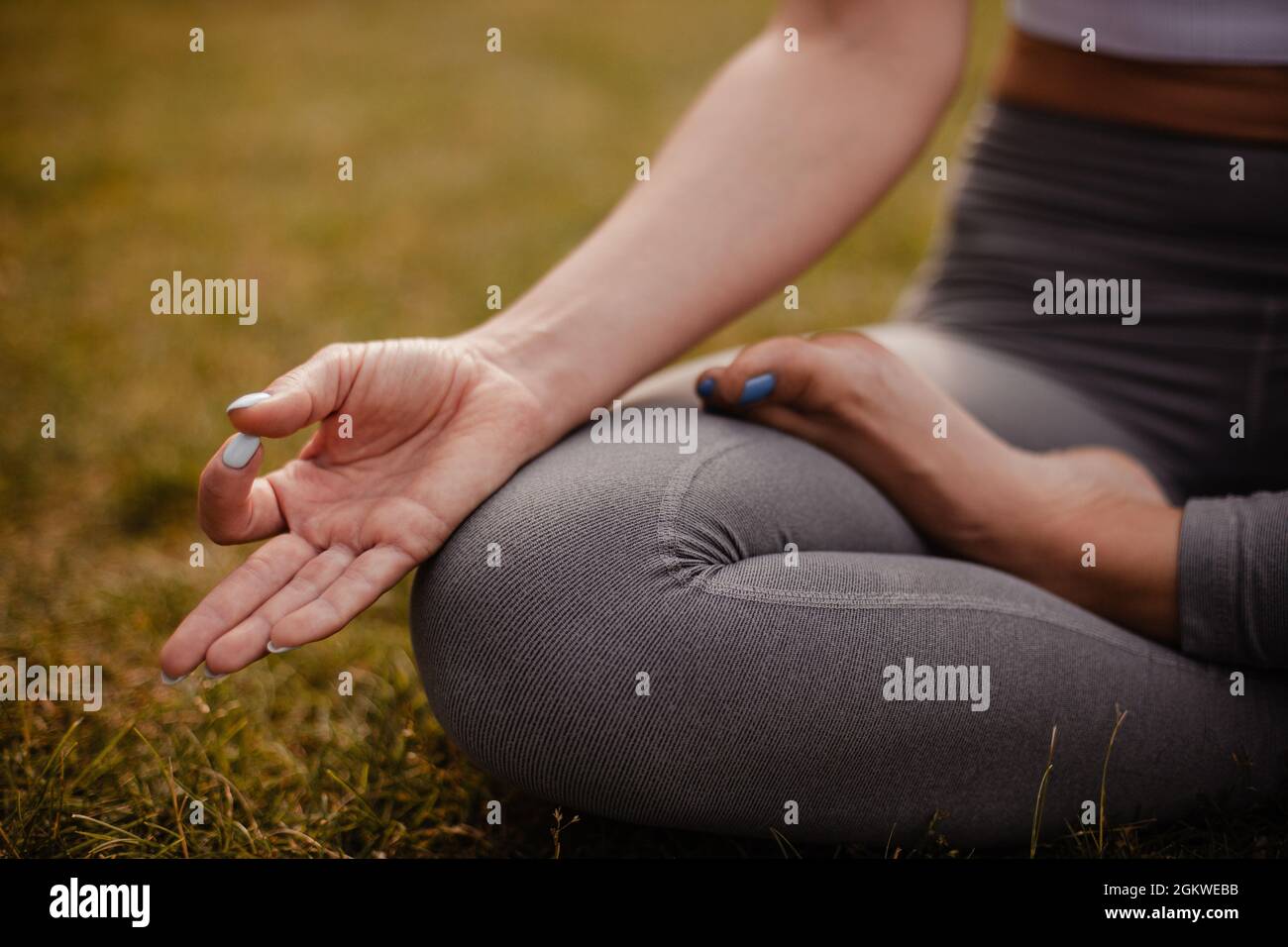 Close - su delle gambe di donna seduta in posizione di loto e meditating e con le dita in mudra Gyan al tramonto in tsummer nella foresta Foto Stock
