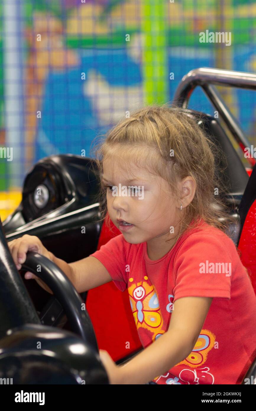 Piccola ragazza caucasica di cinque anni che guida auto in centro giochi all'interno Foto Stock