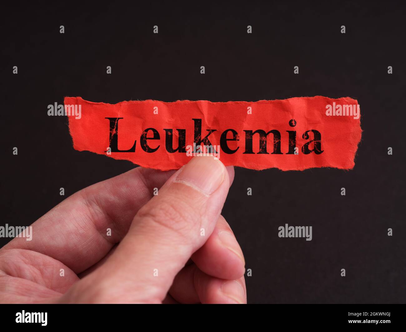 Un uomo che tiene un pezzo di carta rossa con la parola leucemia su di esso. Primo piano. Foto Stock