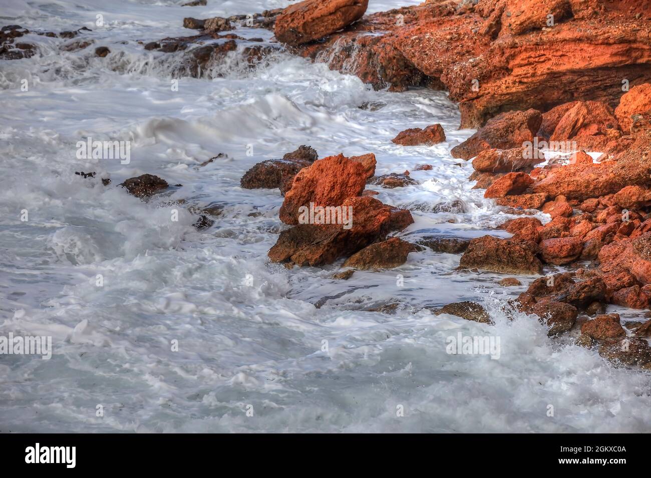 Red Coast Rocks. Acqua salata con schiuma sulla costa dell'isola di Syros, Grecia. Foto Stock