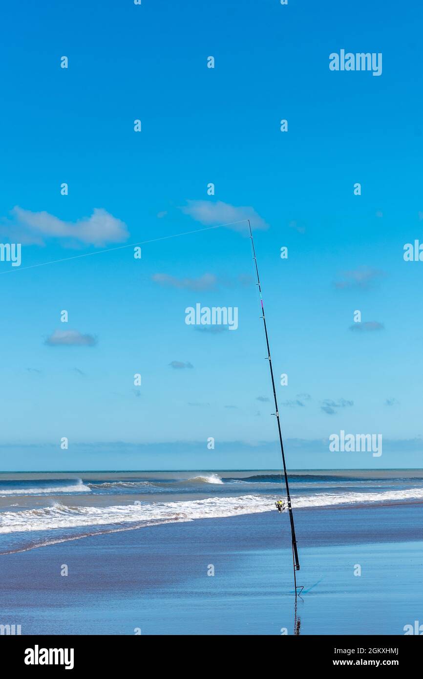 Canna da pesca con mulinello da pesca sulla spiaggia in una bella giornata di sole. Foto verticale Foto Stock