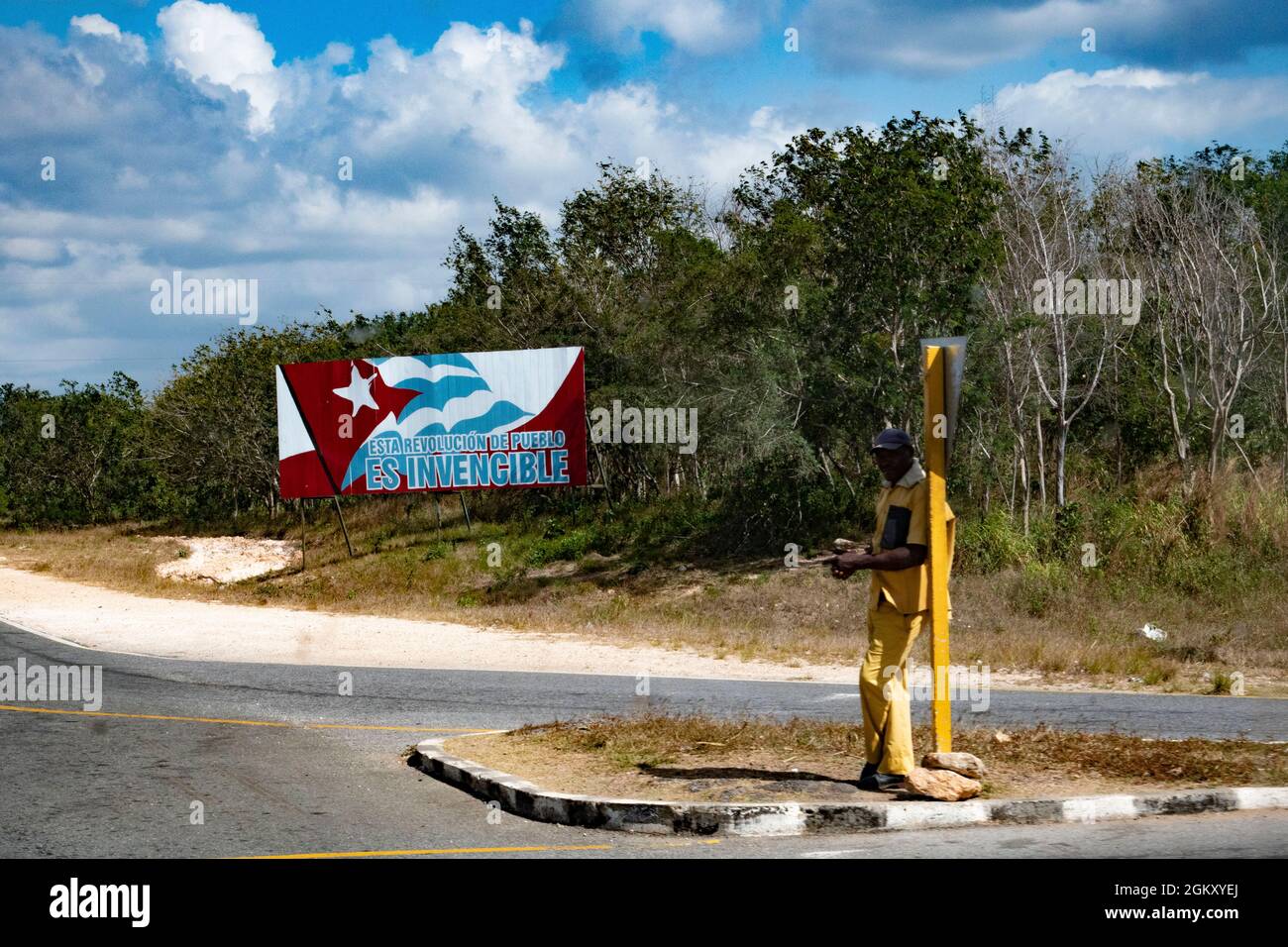 Uomo in piedi sulla strada cubana che perde per un giro a casa in una giornata calda. Foto Stock