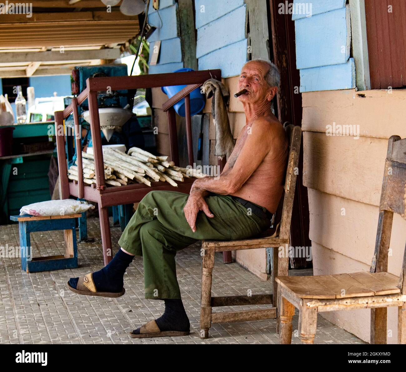 L'uomo siede nel portico anteriore della casa che fuma un sigaro cubano a Trinidad, Cuba. Foto Stock