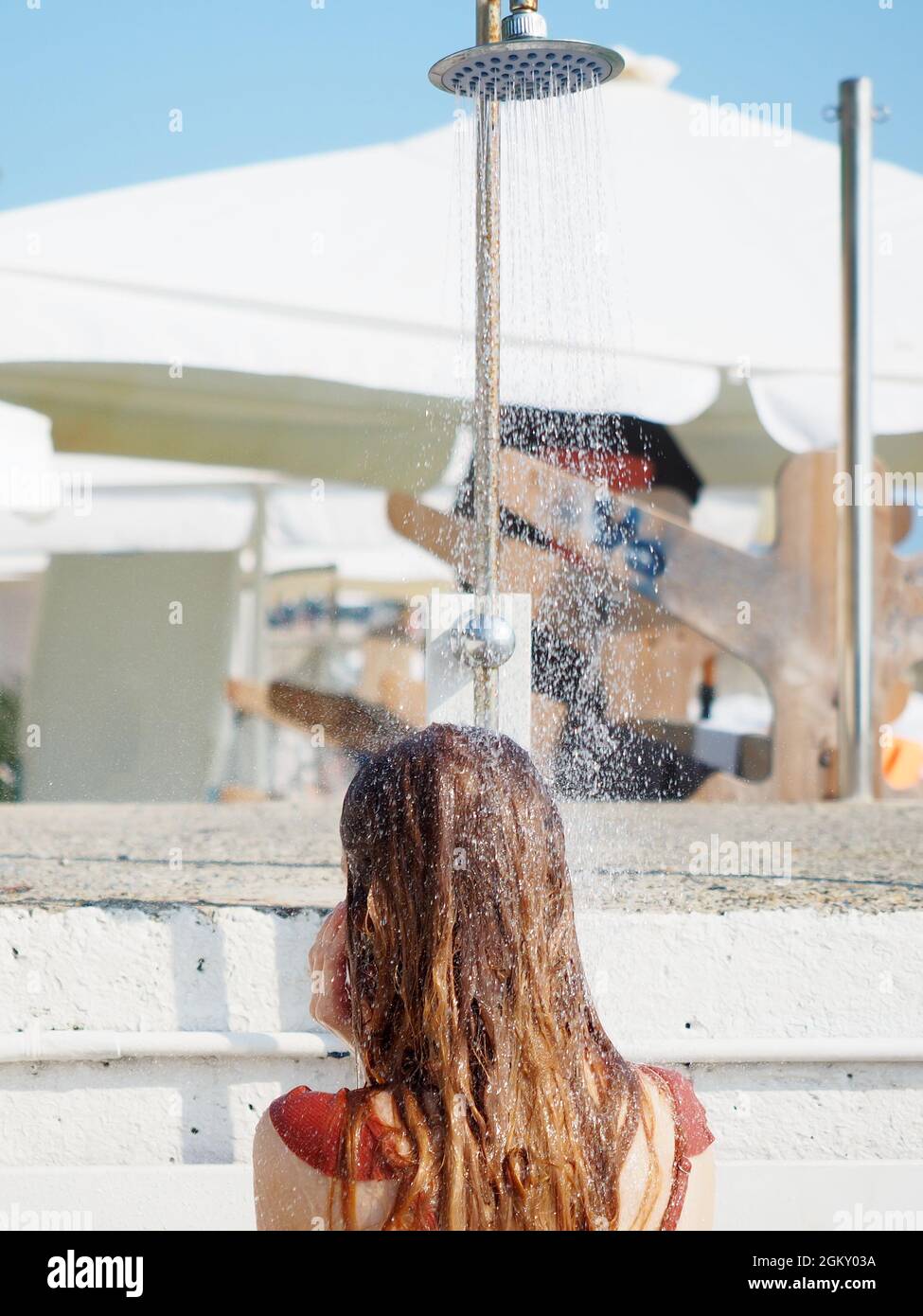 Una ragazza si alza sotto il getto di doccia sulla spiaggia in una giornata  estiva soleggiata. Vista posteriore Foto stock - Alamy