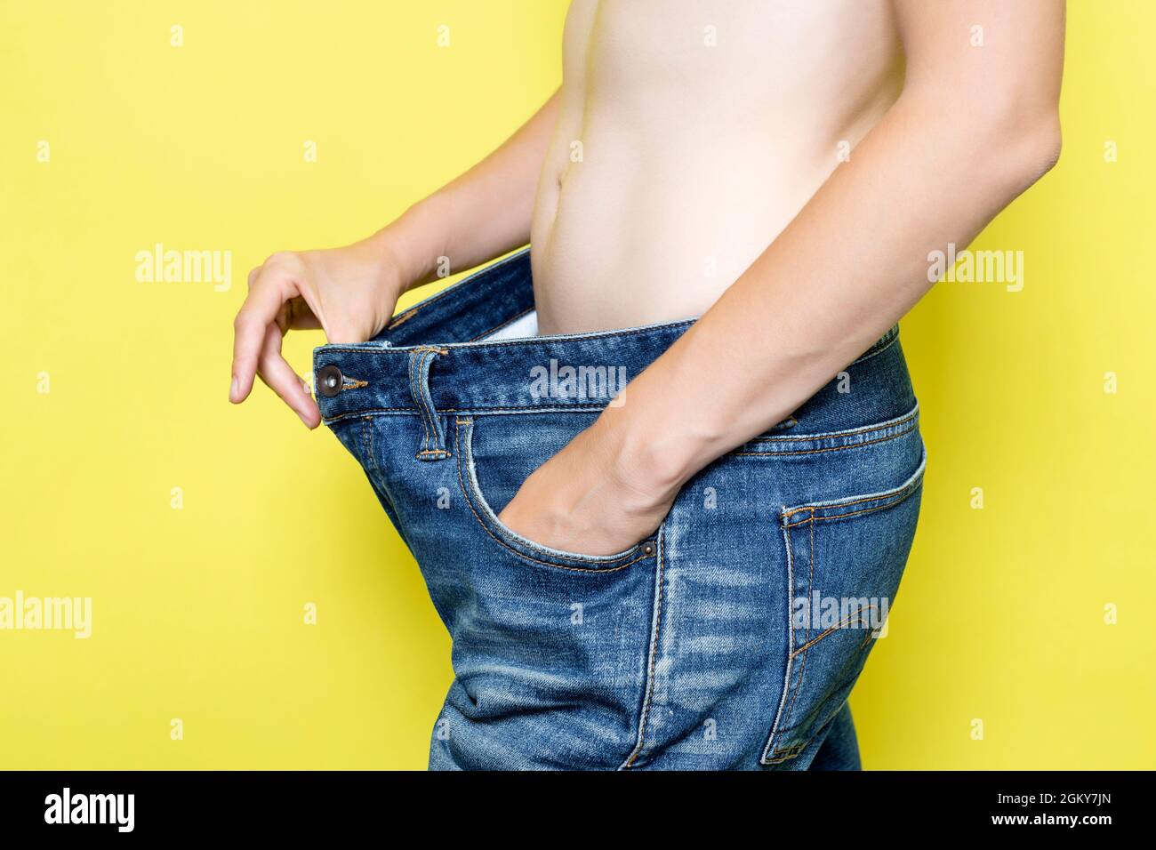 Il concetto di dieta, nutrizione adeguata, perdita di peso. Donna sottile che mostra jeans sciolti e il suo peso di perdita. Donna in jeans oversize isolato sul giallo Foto Stock