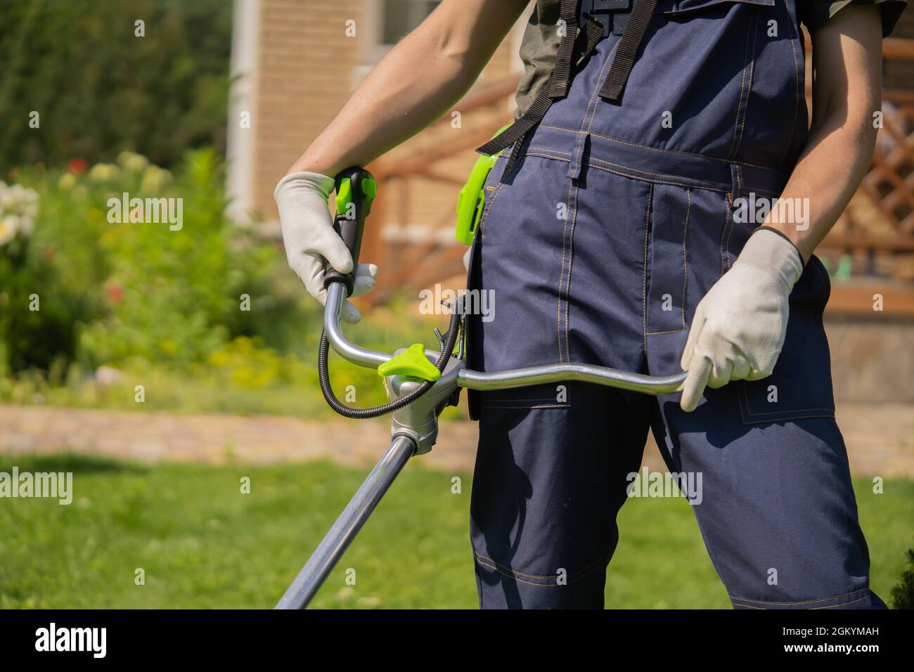 Un primo piano di un giovane bianco che muove un prato con un rasaerba nelle mani Foto Stock
