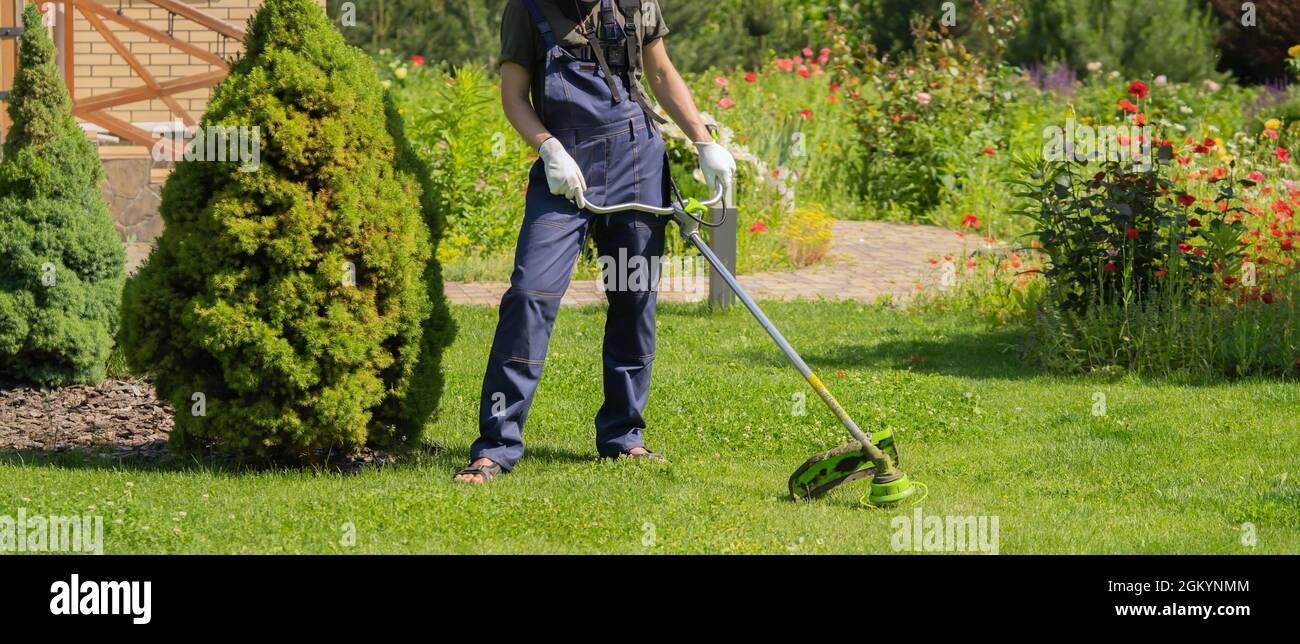 Un giovane uomo bianco sta falciando un prato con un tosaerba nel suo giardino sul retro Foto Stock