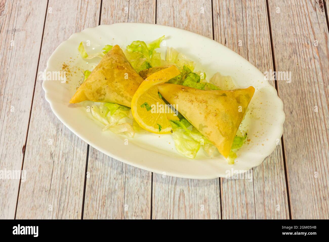 Porzione di samosa vegetale servita in un ristorante indù con lattuga iceberg e una fetta di limone con pepe e curry macinato Foto Stock