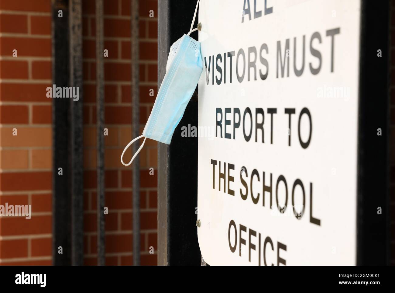 Un segno autentico all'ingresso di una scuola terra un segno che dichiara i visitatori devono riferire al front Office con una maschera protettiva blu appesa Foto Stock