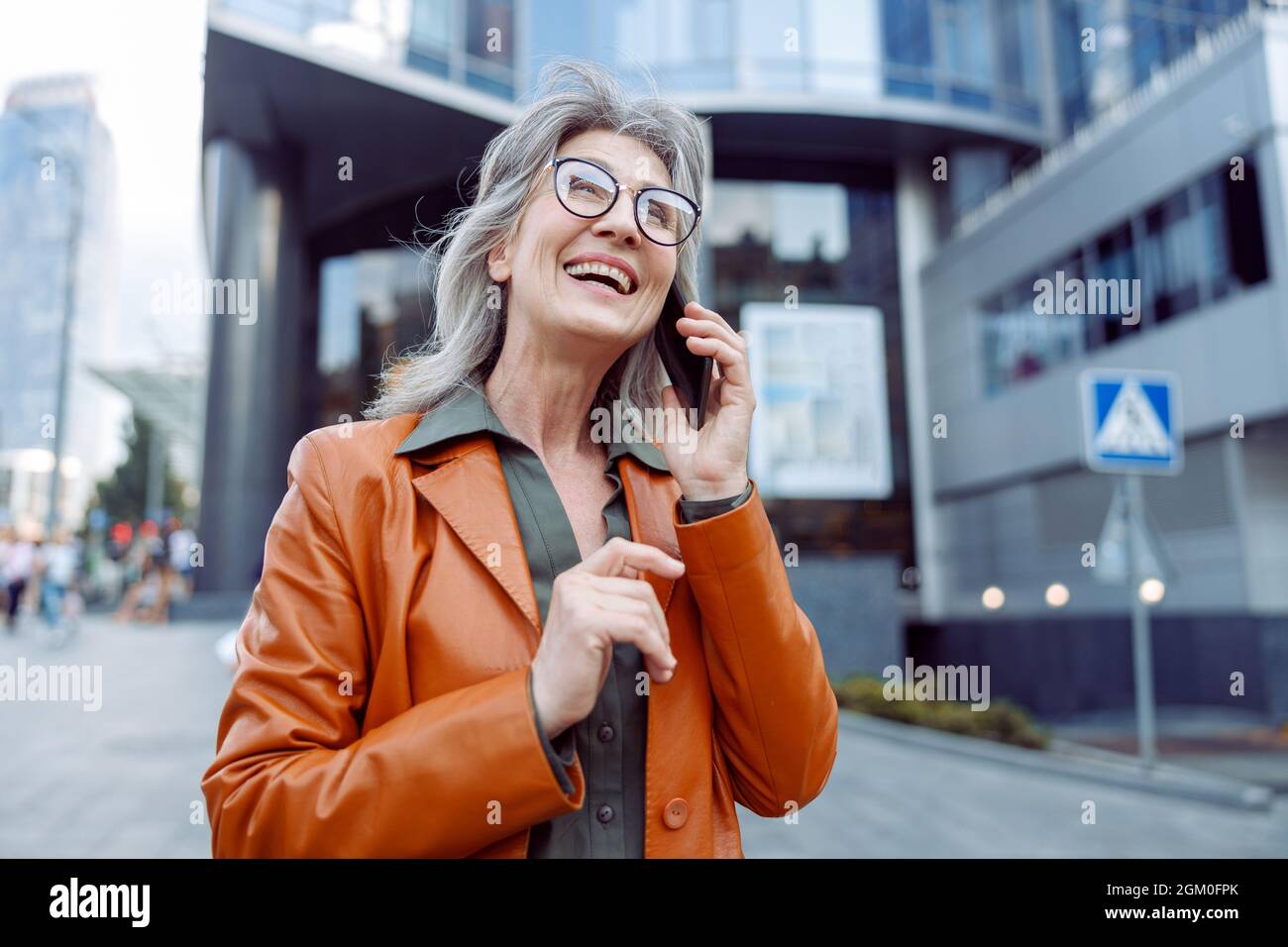 Gioioso hoary haired Senior Lady parla sul cellulare sulla strada moderna della città Foto Stock