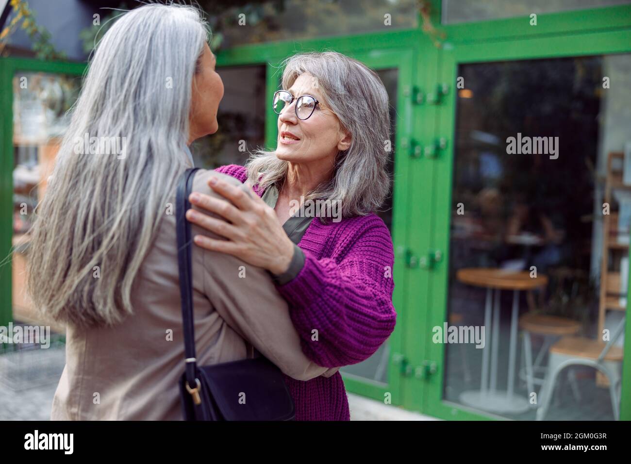 La donna anziana positiva abbraccia l'amico con i capelli grigi riunione sulla strada della città Foto Stock