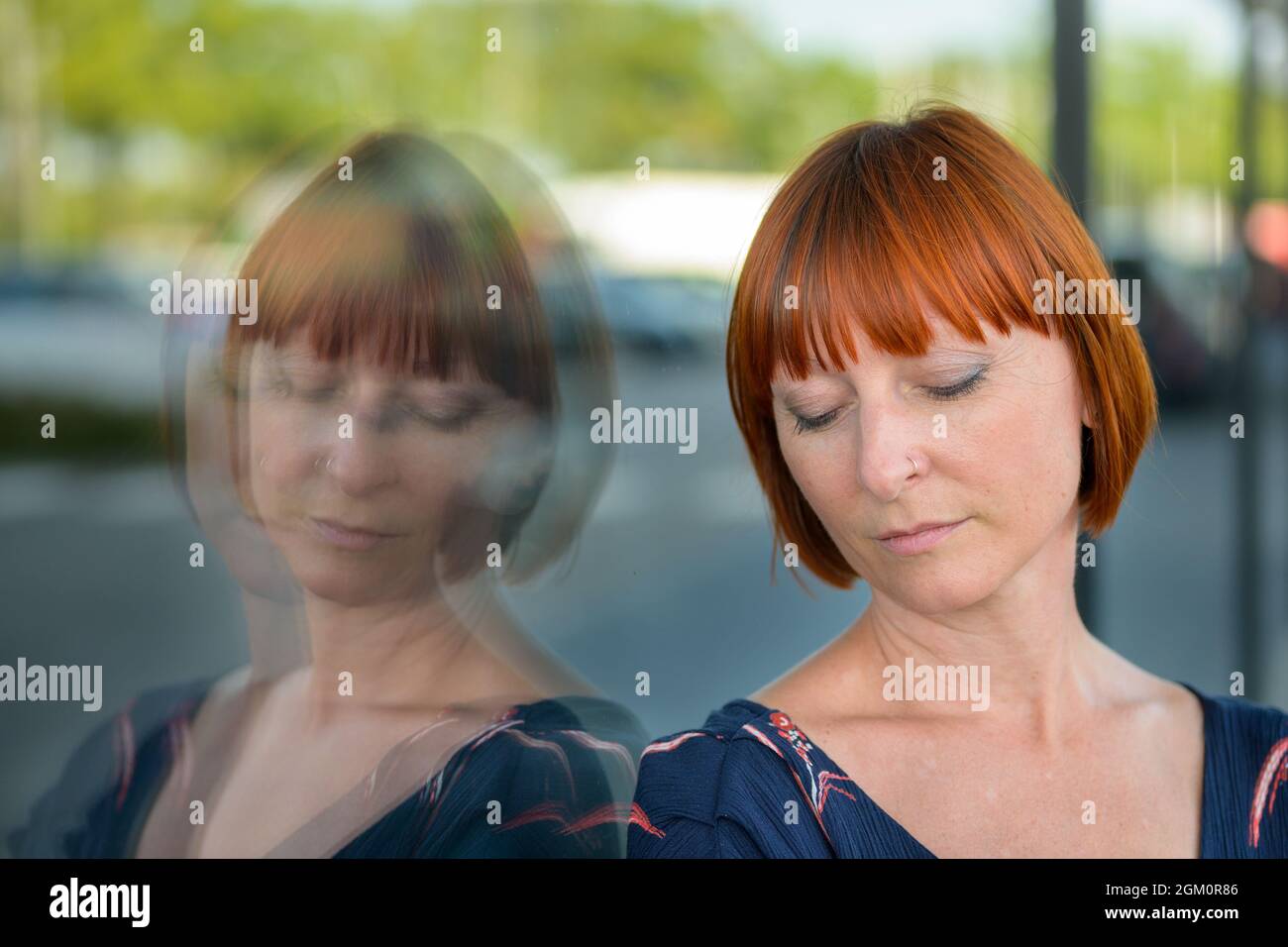 Donna abbattuta con un'espressione triste e occhi downcast in piedi appoggiati contro una vetrina del negozio in città riflesso nel vetro in un colpo di testa in primo piano Foto Stock