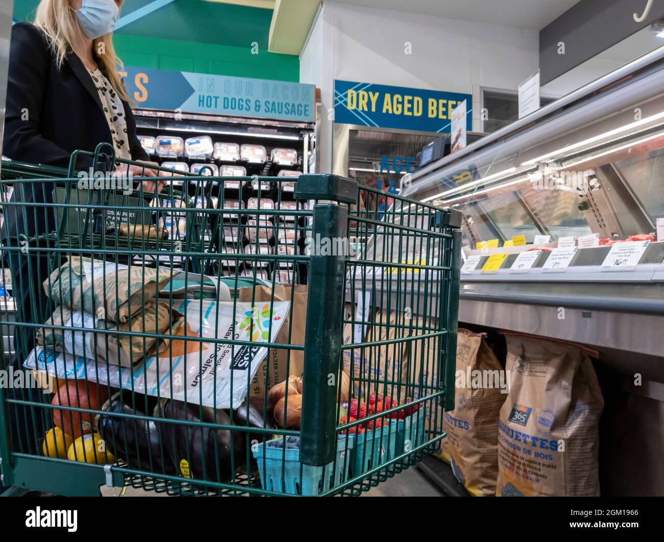 Kirkland WA USA - circa Settembre 2021: Vista di una donna bionda in attesa al banco di carne all'interno di un intero negozio di alimentari Foods Market, spingendo un pieno s Foto Stock Kirkland WA USA - circa Settembre 2021: Vista di una donna bionda in attesa al banco di carne all'interno di un intero negozio di alimentari Foods Market, spingendo un pieno s Foto Stock