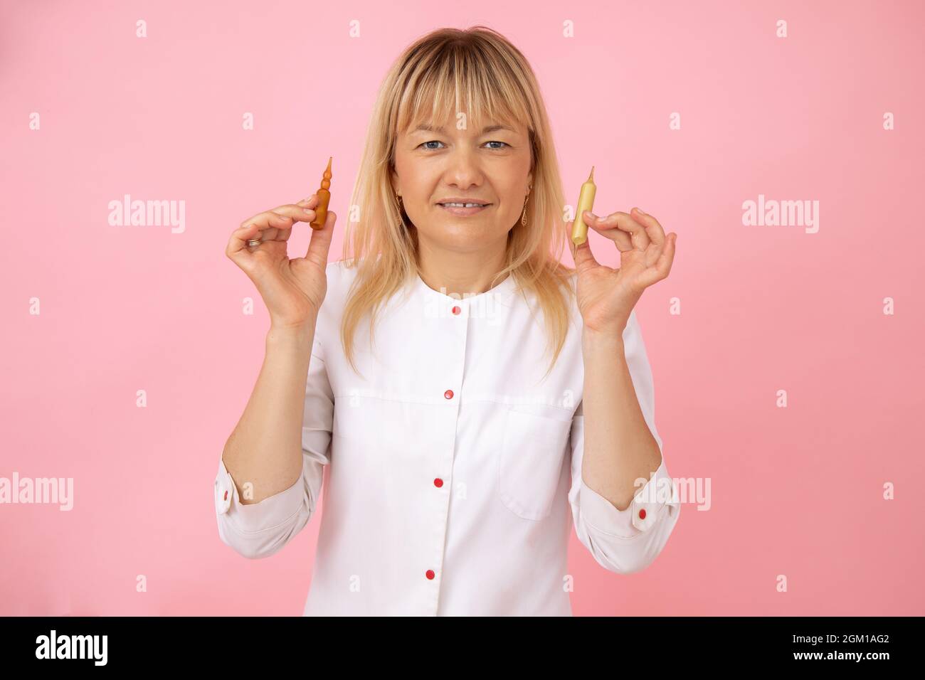 Il cosmetologo biondo in uniforme medica bianca tiene le capsule per le procedure cosmetiche nelle sue mani. Piccola impresa. Salone DI BELLEZZA. Industria di bellezza. Foto Stock