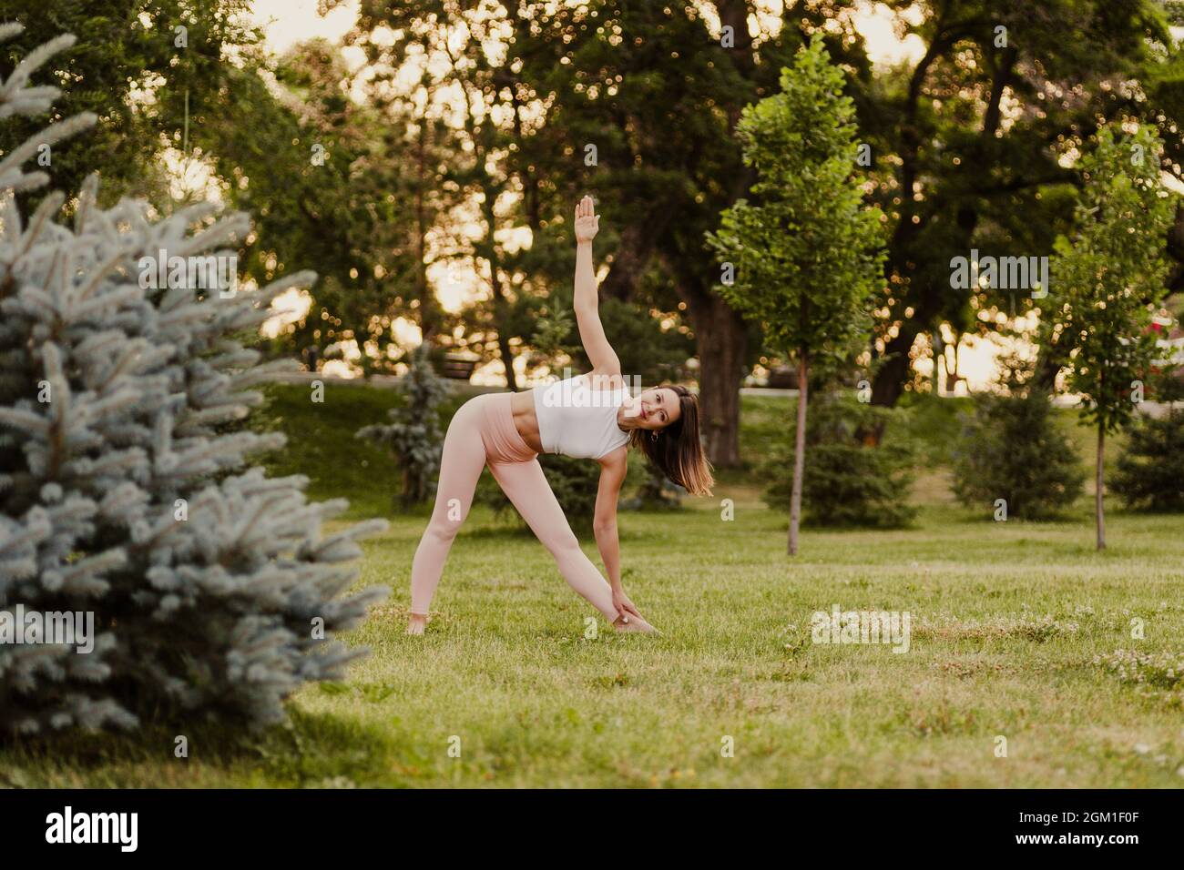 donna tranquilla, in piedi in posa triangolare e fare yoga al tramonto nel parco in estate, concetto di meditazione e contemplazione Foto Stock