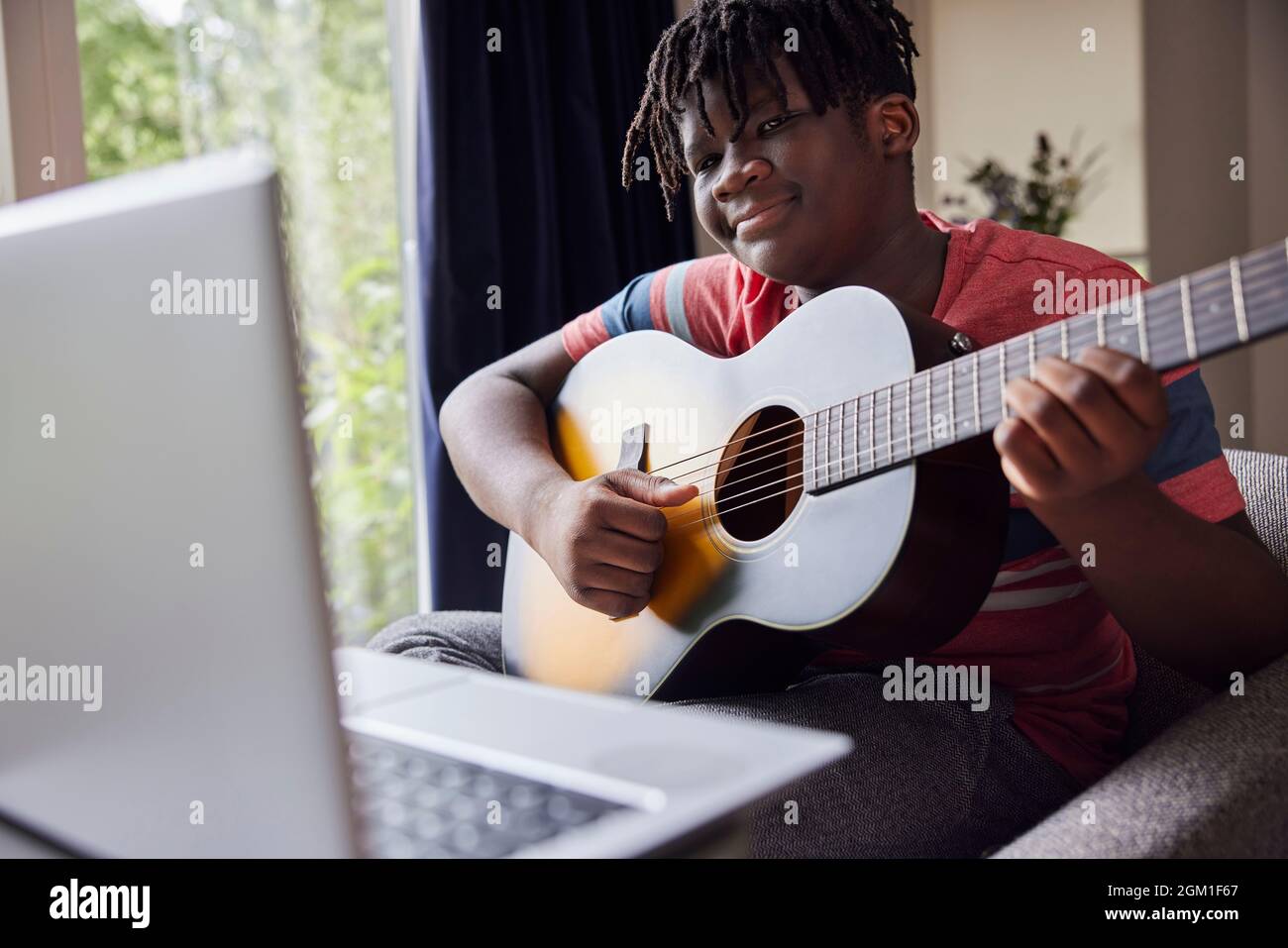 Teenage Boy imparare a giocare chitarra Acosutic con lezione online su computer portatile a casa Foto Stock