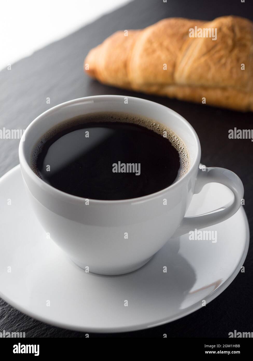 Tazza di caffè e croissant su sfondo nero ardesia Foto Stock