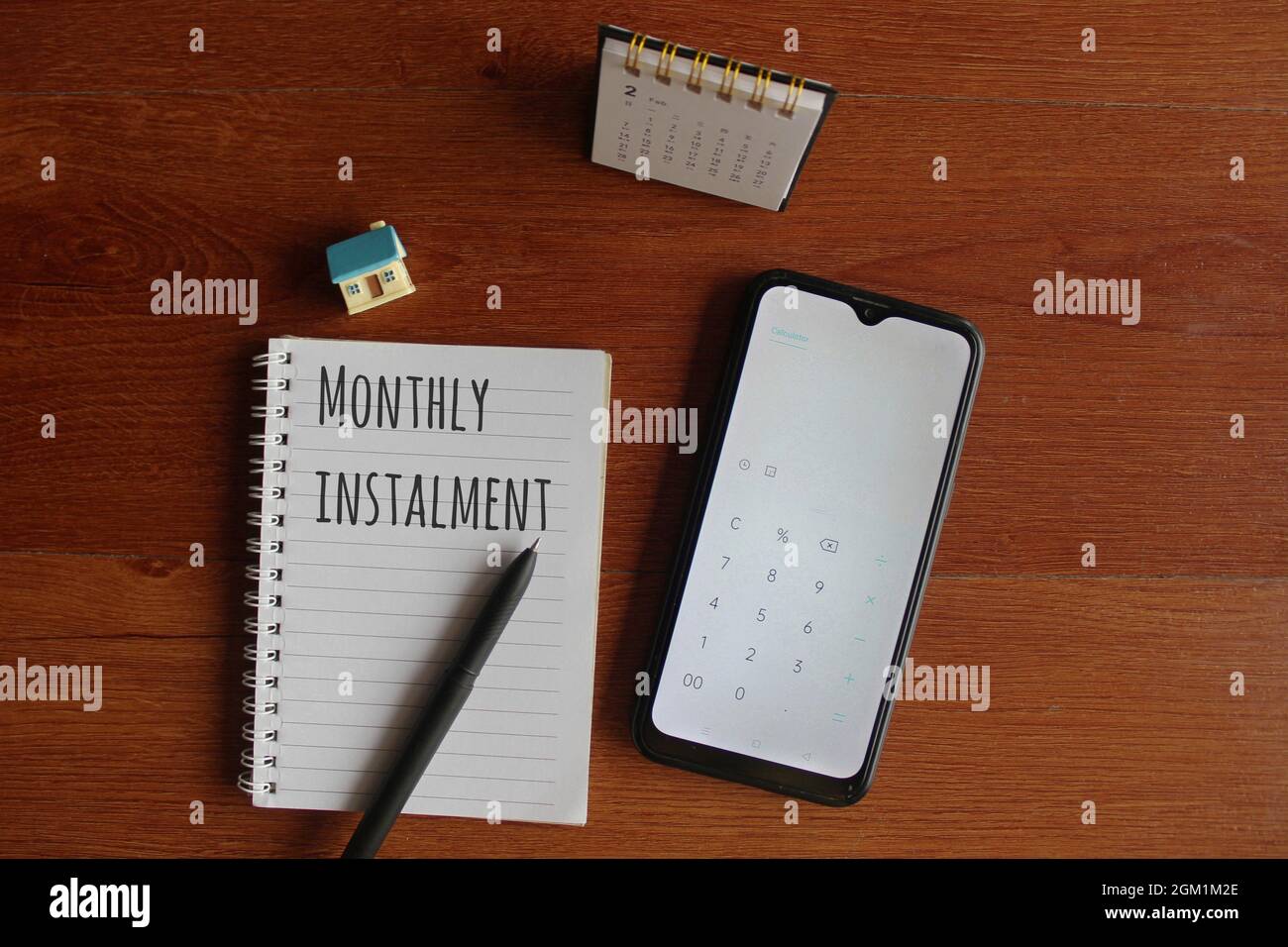 Finanza, concetto di calcolo. Vista dall'alto del calendario della scrivania, della calcolatrice su smartphone, della casa in miniatura e del notebook scritti con UNA RATA MENSILE di testo Foto Stock