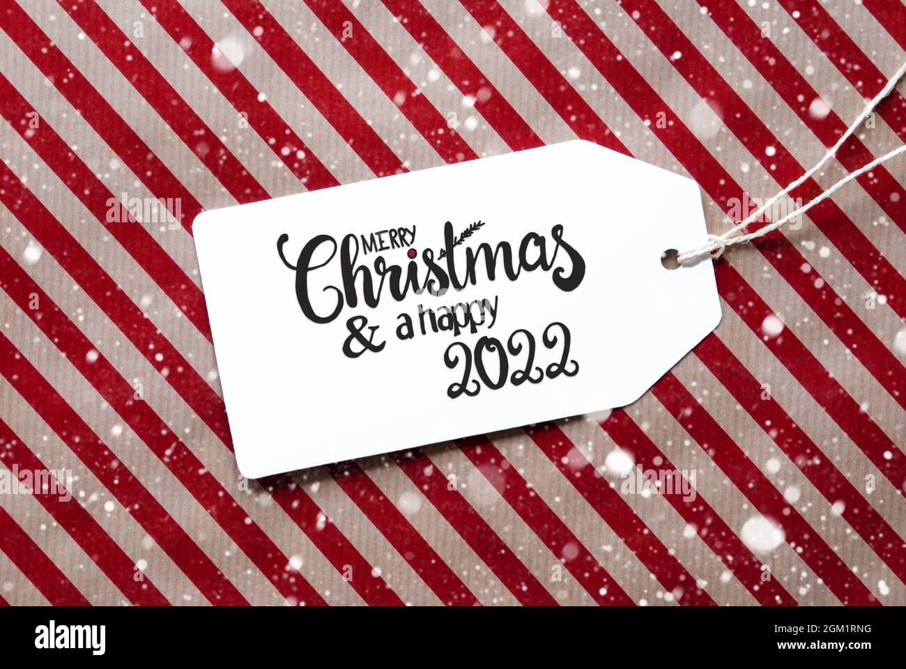 Etichetta con calligrafia inglese buon Natale e un felice 2022. Carta da imballaggio rossa come sfondo con fiocchi di neve Foto Stock