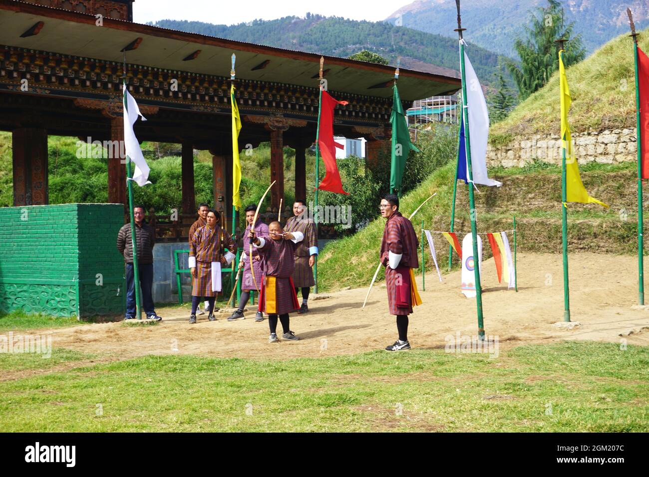 Gli arcieri bhutanesi guardano come un compagno di squadra si allinea al suo prossimo colpo a Thimphu, Bhutan. Il tiro con l'arco è lo sport nazionale del Regno del Bhutan. Foto Stock