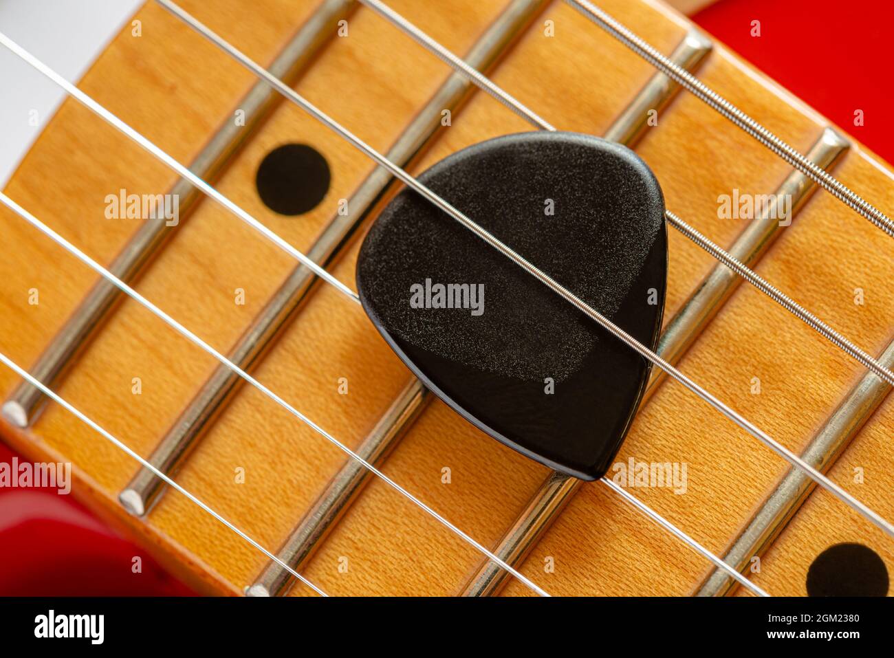 Dettaglio del collo e delle corde di una chitarra elettrica rossa, con un plectrum nero chiamato anche mediatore Foto Stock