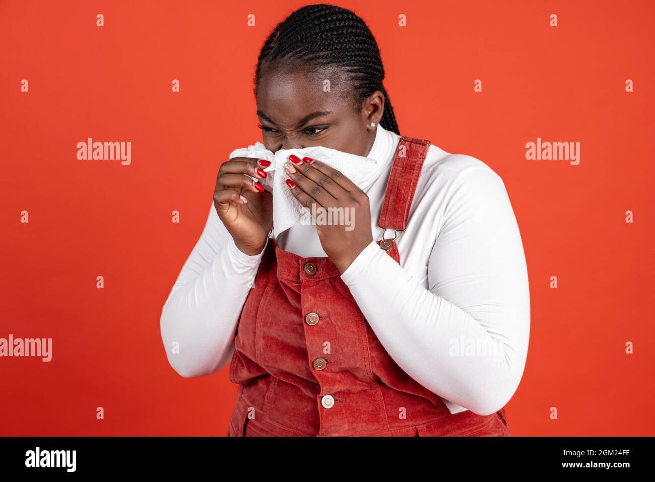 Ritratto di donna malata africana starnutire isolato su sfondo rosso studio. Concetto di emozioni umane, espressione facciale, bellezza naturale, bodypositive Foto Stock