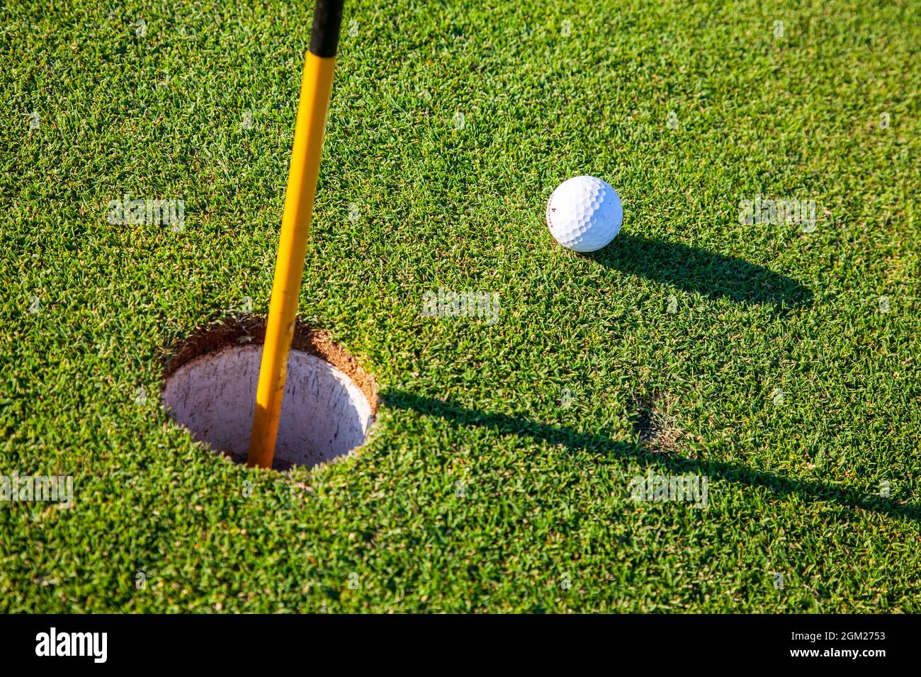 Palla da golf sul putting green da buco e bandiera. Ombre lunghe. 2008 Foto Stock