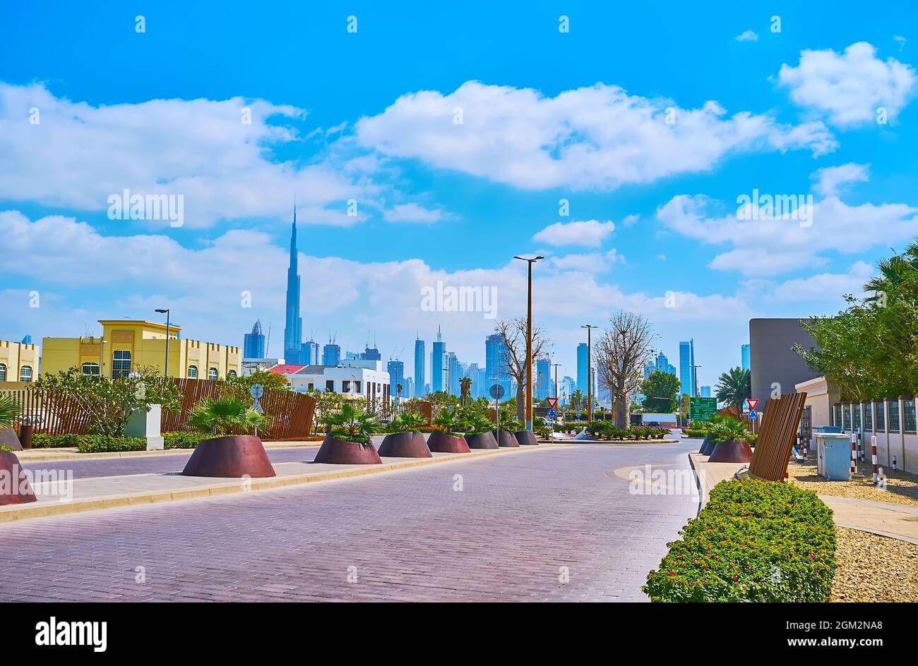 La strada panoramica e verde di Jumeirah è decorata con piante verdi e vanta la vista sull'iconico skyline di Dubai con Burj Khalifa e altri grattacieli Foto Stock