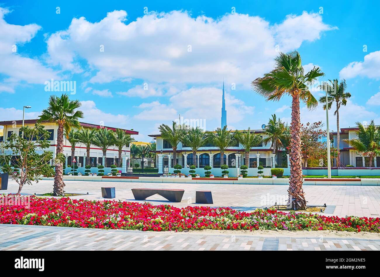 Le moderne case in al Urouba strada, decorate con aiuole di fiori, palme, futuristiche panchine, la guglia di Burj Khalifa è visto in background, Dubai, Foto Stock