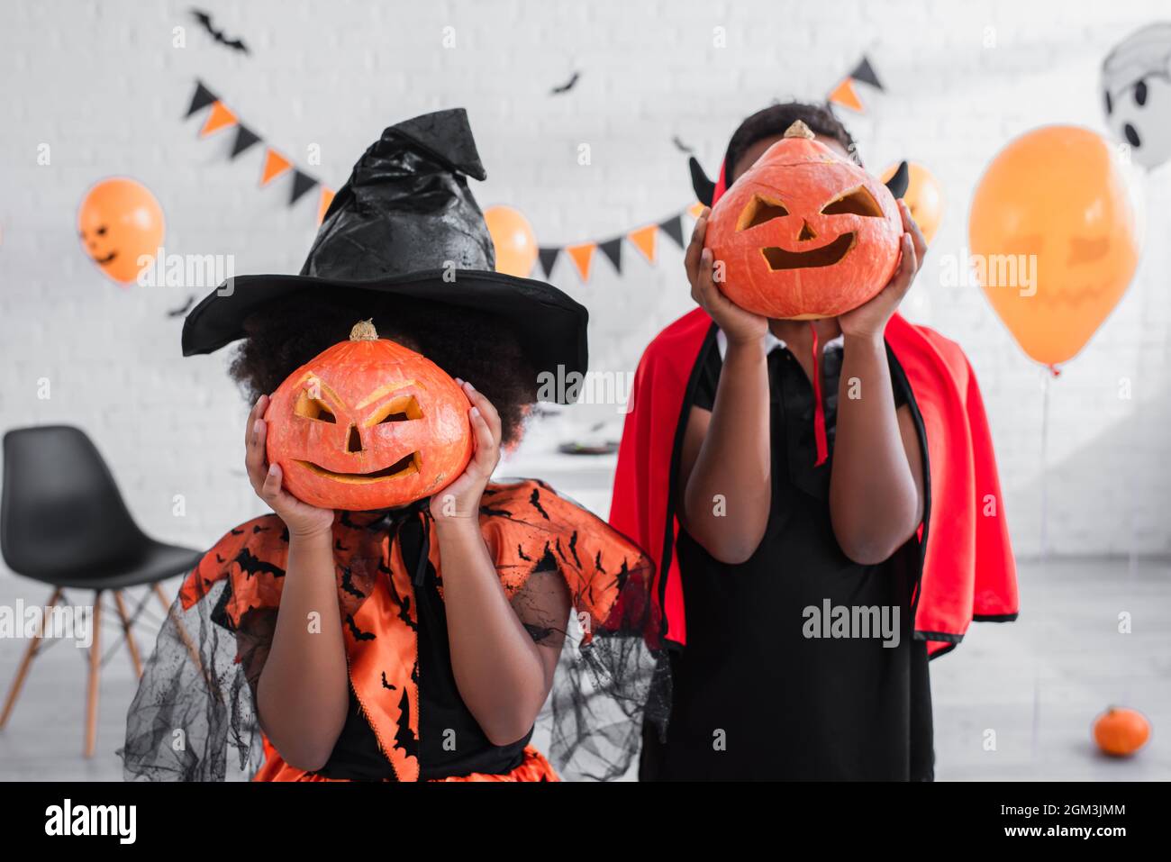 bambini afroamericani in costumi di halloween che coprono i volti con zucche scolpite a casa Foto Stock