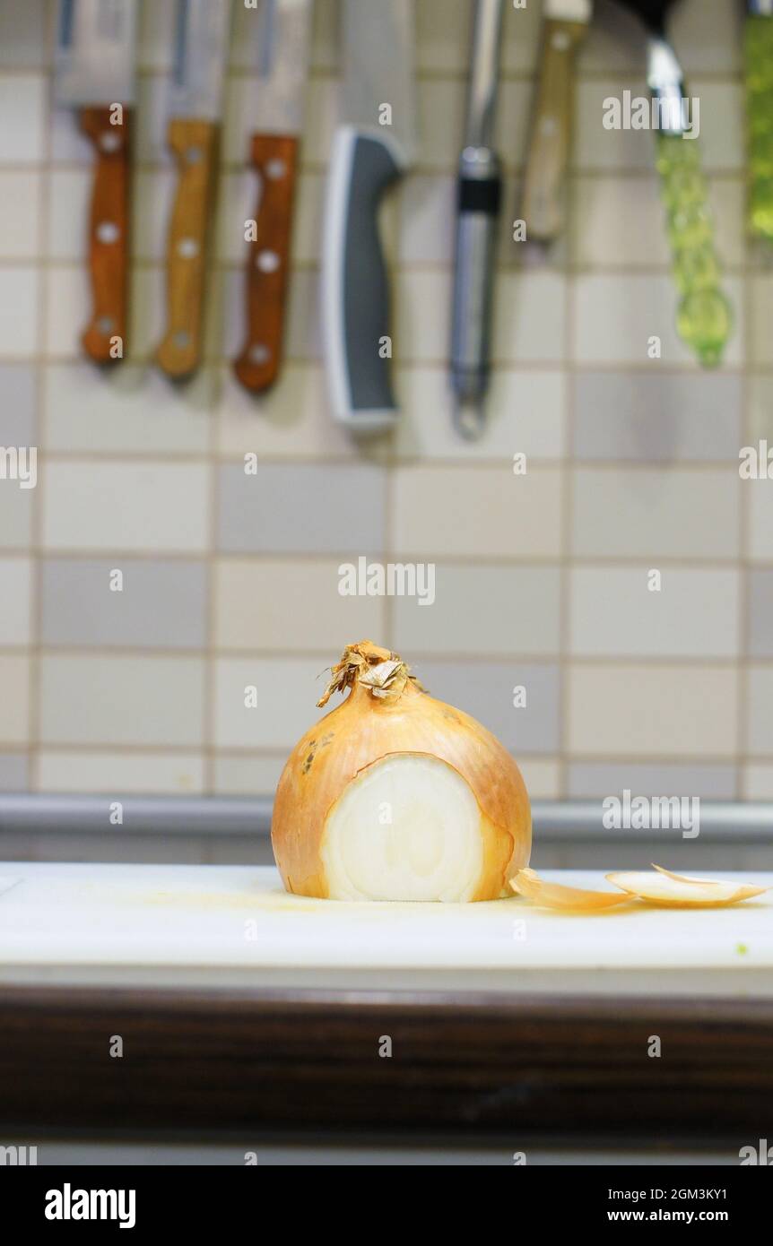 Colpo verticale di cipolla tagliata sullo sfondo di una parete piastrellata con coltelli in cucina Foto Stock