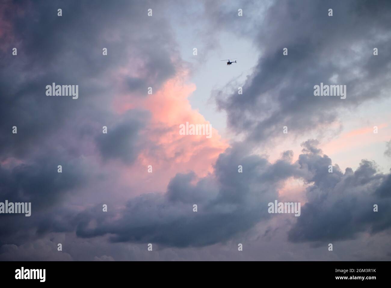 Vista delle nuvole rosa e viola pastello con elicottero a oggetto singolo che vola nell'abisso. Vista artistica del cielo Foto Stock