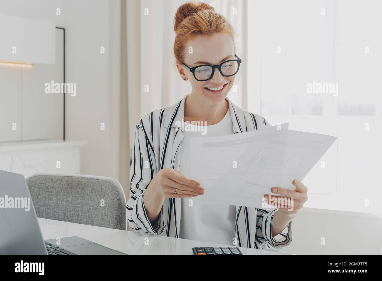Felice sorridente donna caucasica leggere buone notizie in documenti finanziari mentre la gestione del bilancio di famiglia Foto Stock