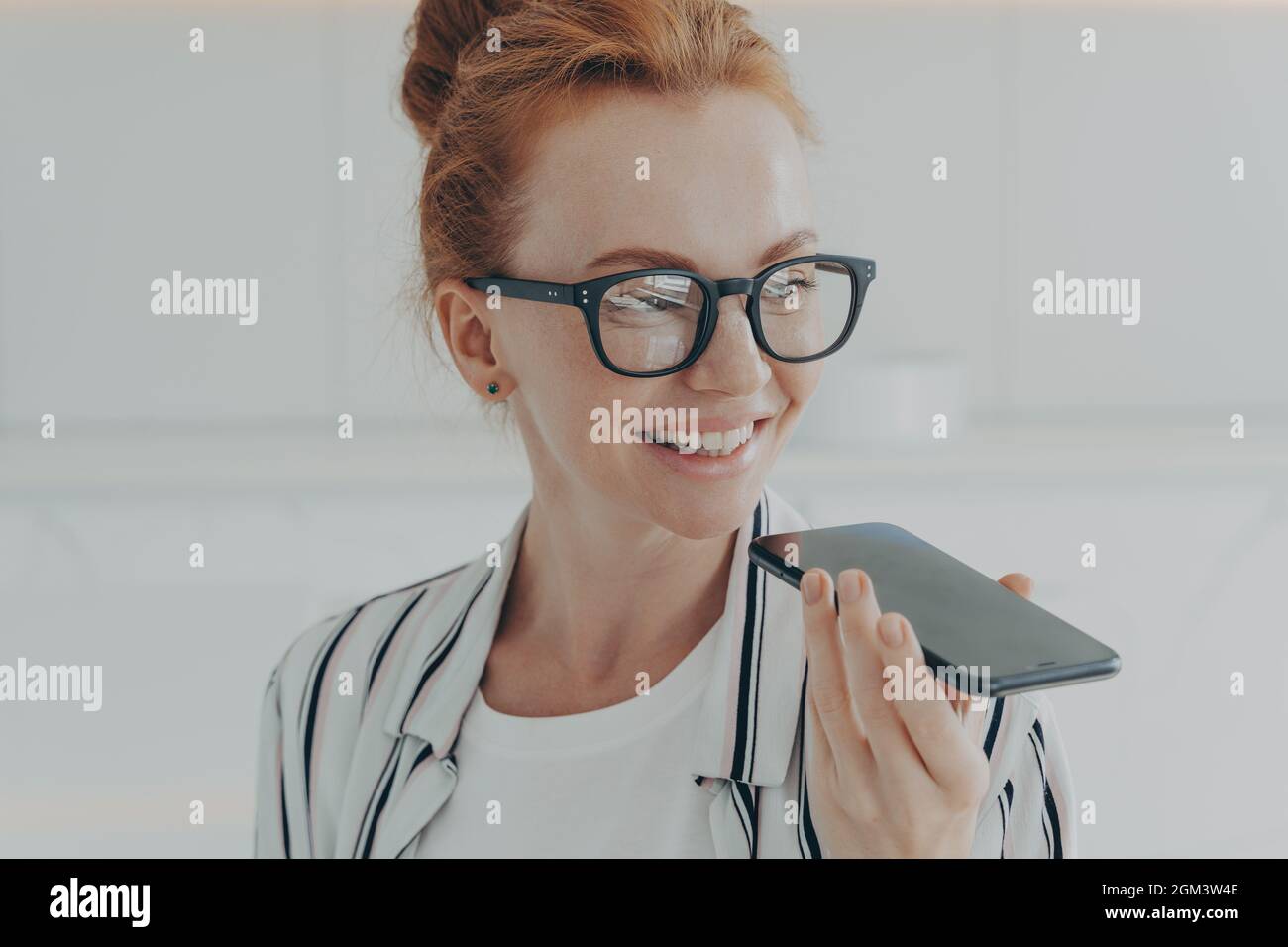 Ritratto di felice allegra donna rossa-capelli in occhiali tenendo cellulare, registrazione messaggio audio Foto Stock