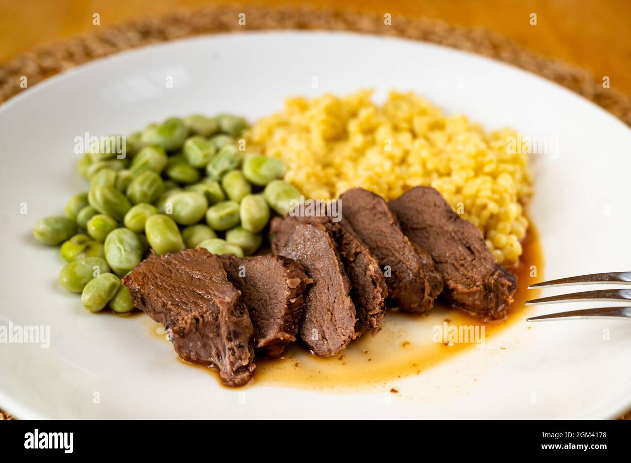 Affettati di cervi magri, fave bollite e pasta di semola tarhona sul piatto con forchetta, primo piano. Foto Stock