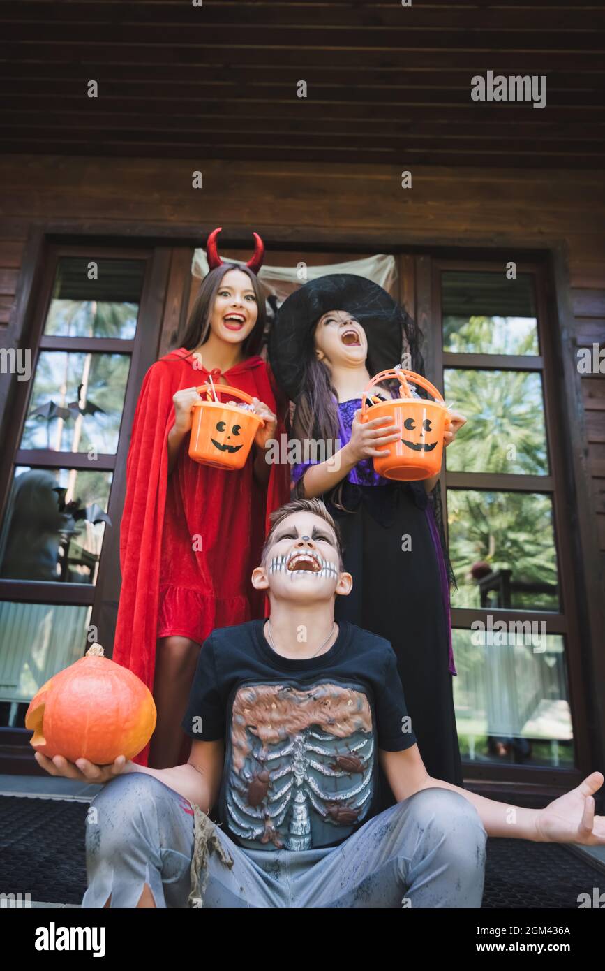 i capretti eccitati nei costumi spaventosi di halloween che tengono i  secchi con i dolci e urla sul portico Foto stock - Alamy