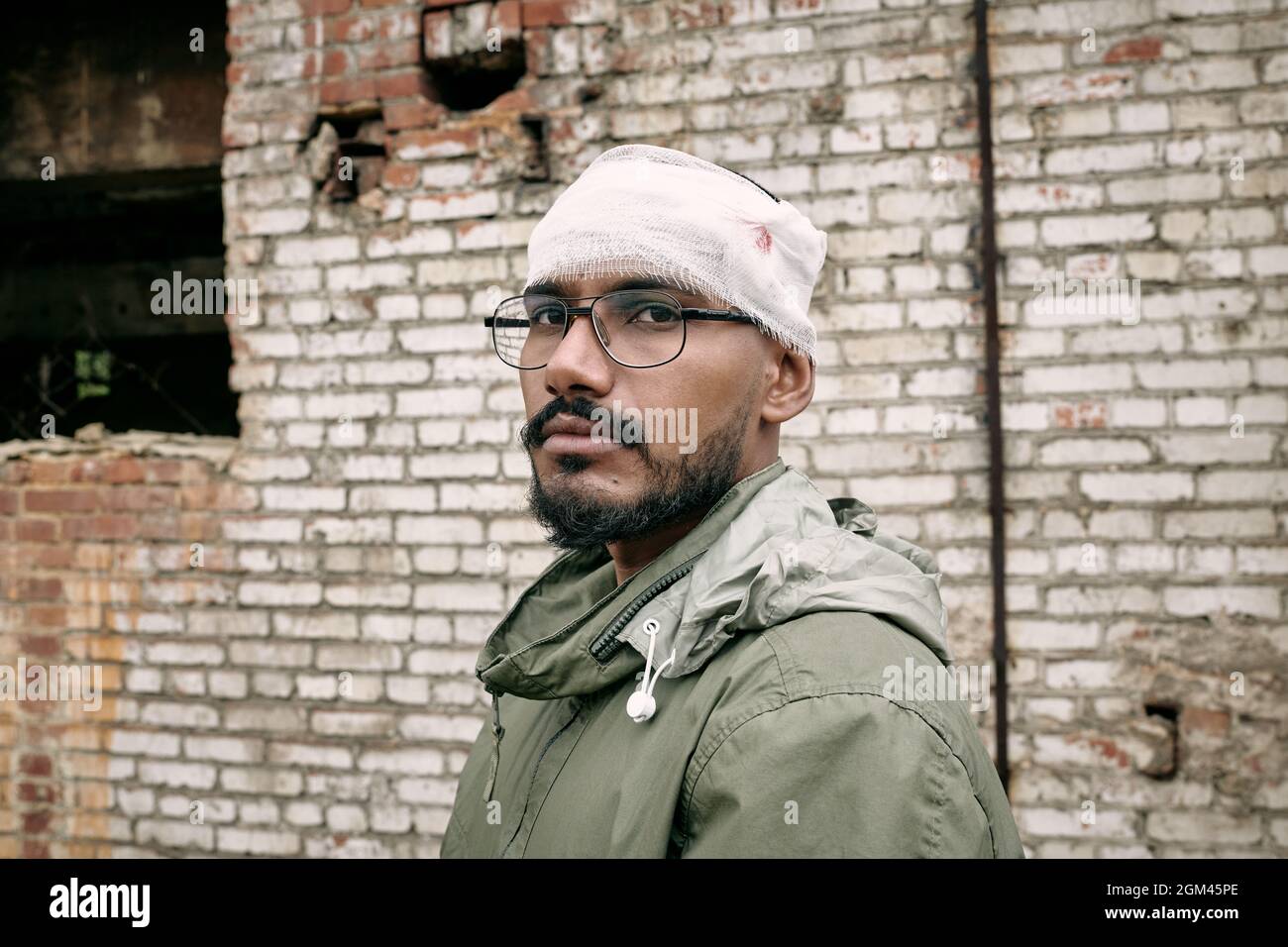 Ritratto di miserabile giovane medio-orientale uomo con barba con testa bandita, edificio abbandonato in background Foto Stock