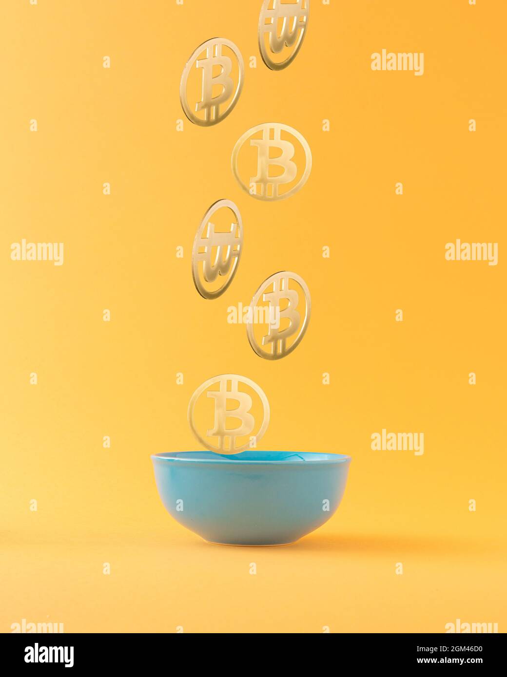 Bitcoins cadendo in ciotola blu su sfondo arancione. Concetto di ricchezza Bitcoin. Tecnologia mineraria o blockchain per il concetto di criptovaluta. Astratto Foto Stock