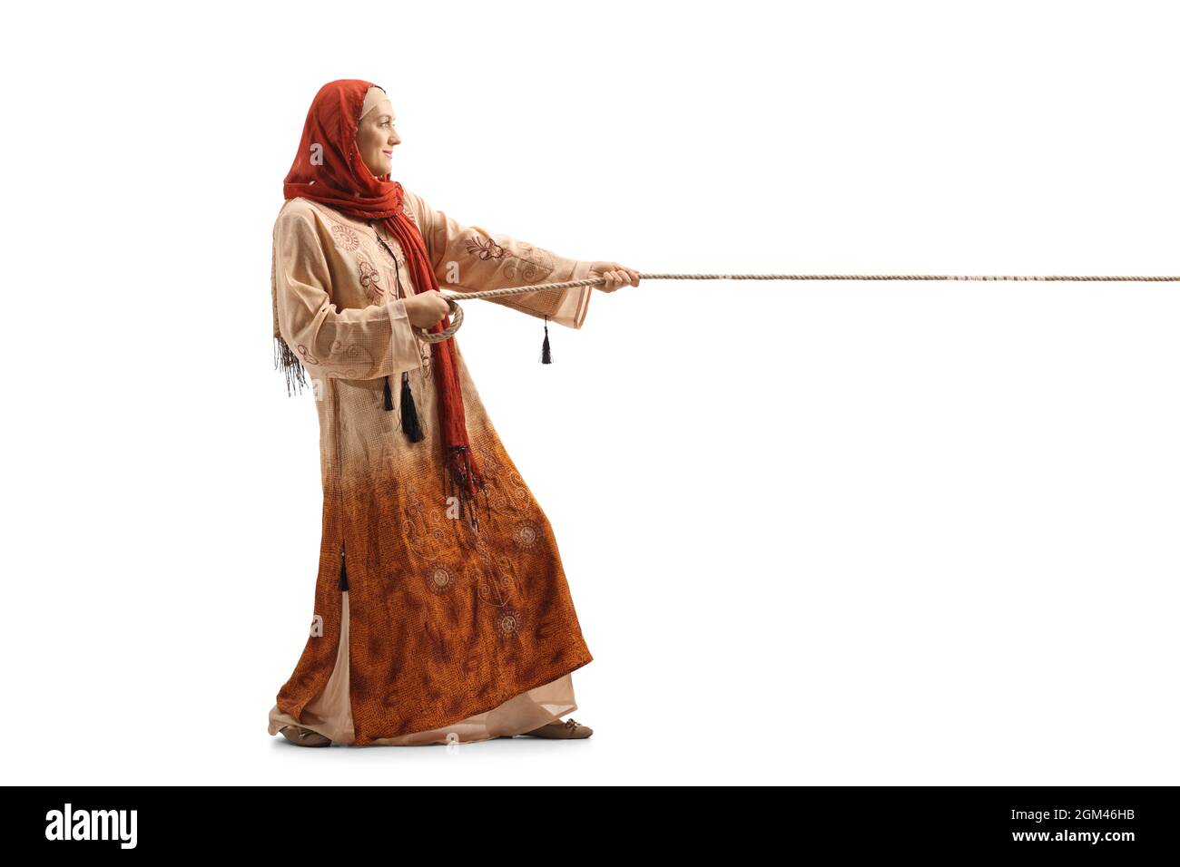 Colpo di profilo a tutta lunghezza di una donna in abiti etnici e hijab tirando una corda isolata su sfondo bianco Foto Stock
